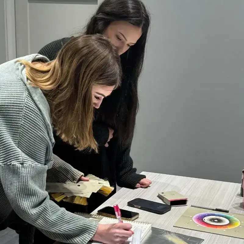 Two women examining samples and writing on a notepad at a design meeting.