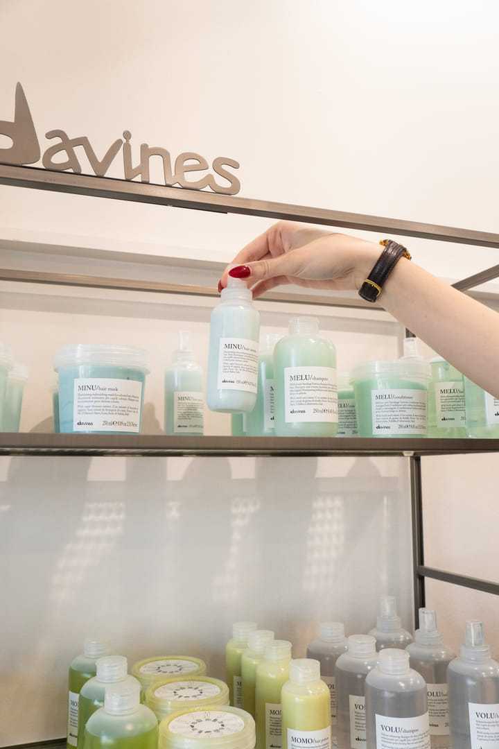 Hand reaching for Davines hair product on a shelf with various bottles displayed.